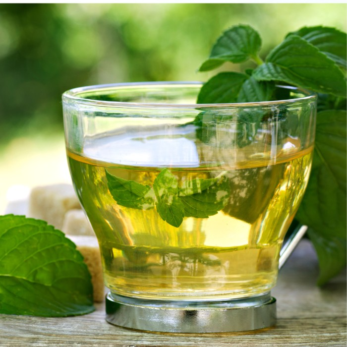 A glass of mint tea with mint leaves around it.